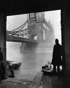 a man standing on the side of a river next to a bridge