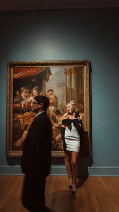 a woman in a white dress standing next to a man with a painting behind her