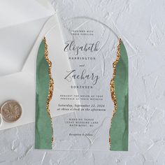 a white and green wedding card with gold foil on the front, next to an envelope