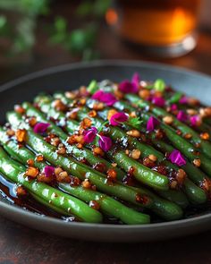 a black plate topped with green beans covered in sauce and garnished with pink flowers