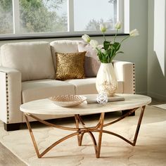 a living room with a couch, coffee table and flowers in a vase on the floor