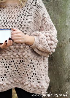 a woman is holding a cup in her hands while wearing a crocheted sweater