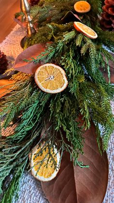 an arrangement of oranges, pine cones and evergreen branches on top of a table