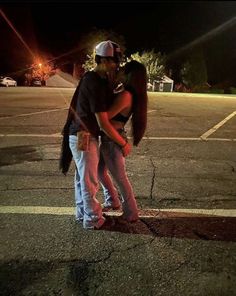 a man and woman standing in the middle of an empty parking lot with their arms around each other