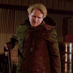 a man in a green jacket standing next to some metal containers and looking at the camera