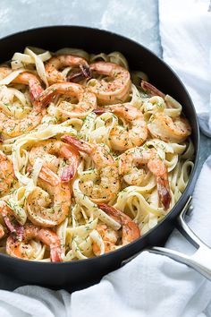 a skillet filled with shrimp and pasta on top of a white towel next to a fork