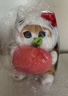 a small toy cat holding a large red object in it's mouth and wearing a santa hat