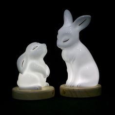 two white ceramic rabbits sitting on wooden bases