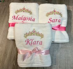 three white towels with pink bows and tiaras on them, sitting on a wooden floor