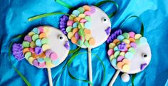 three lollipops decorated with colorful candies on a blue cloth covered table