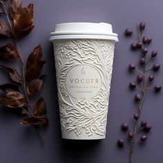 a coffee cup sitting on top of a table next to some purple berries and leaves