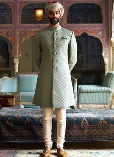 a man in a green outfit standing next to a blue couch and ottomans, with his hands on his hips