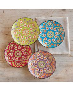 four colorful plates sitting on top of a wooden table next to a white towel and napkin