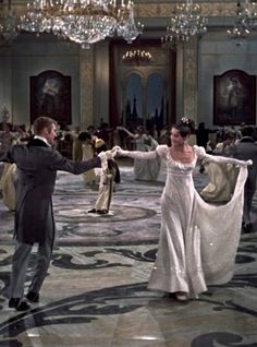 a man and woman dancing in a ballroom with chandeliers hanging from the ceiling