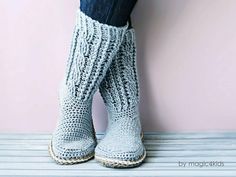 the legs of a woman wearing crochet knitted boots, standing against a pink wall