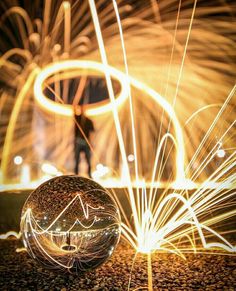 a person standing next to a glass ball with firework in the air behind it