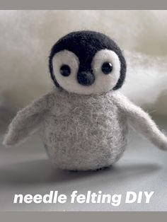 a needle felt penguin sitting on top of a pile of white wool with the words needle felting diy written below it