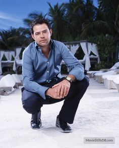 a man sitting on the ground with his hands in his pockets and wearing a blue shirt