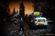 a man standing in front of a school bus covered in snow at night with the lights on