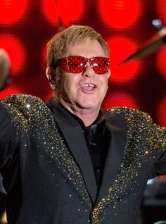 the man is wearing red sunglasses and singing on stage with his hands in the air