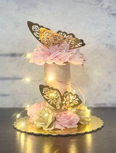 a cake decorated with butterflies and flowers on a plate, lit up by fairy lights