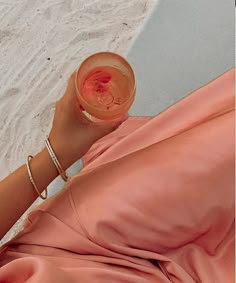 a woman holding a wine glass in her right hand on the beach with white sand