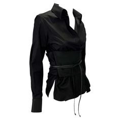 Presenting a stunning black collared Gucci belted shirt, designed by Tom Ford. From the Fall/Winter 2002 collection, this beautiful top features a plunging neckline, collar, and built-in wrap-around obi belt. The top is kept closed by the belt which is secured by a braided leather tie. Obi belts and Japanese influence were heavily present in this dark rocker-chic Gucci by Tom Ford collection, making this top a must-have! Approximate measurements: IT38 23.5" shoulder to hem 23" shoulder to cuff 18" armpit to cuff 3" collar 6" thick obi belt 29" long obi belt (not including braided leather) 100% cotton Elegant Gucci Luxury Shirt, Luxury Gucci Tops With Button Closure, Gucci Long Sleeve Party Tops, Gucci Black Collared Top, Gucci Fitted Luxury Blouse, Classic Gucci Formal Shirt, Tom Ford Style, Gucci By Tom Ford, Ford Black