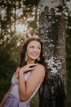 a woman standing next to a tree with her hand on her shoulder and smiling at the camera