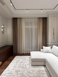 a living room with a large white couch in front of a curtained window and wooden floor