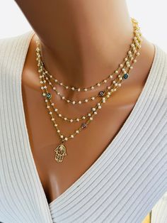 This is a gorgeous 14 karat gold filled multi strand pearl necklace. This necklace features a 14 karat gold filled Hamsa pendant that measures 22X 18 MM. Pearls measure 3 to 3.5 MM. Beautiful colorful Marano glass Evil eye connectors are scattered on this necklace. Spring clasp in back connects all four strands. This necklace is much more stunning in person. Model is wearing the 15 to 18 inch length. Longer lengths available and drop-down list. This necklace may also be ordered in 925 sterling silver version, not shown. Comes in a gift box ready to present. Person Model, 14kt Gold Jewelry, Hamsa Necklace Gold, Multi Strand Pearl Necklace, Pearl Necklace Gold, Necklace Evil Eye, Clean Sterling Silver, Necklaces Women, Gold Hamsa