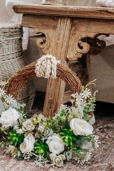 a wreath with white flowers and greenery on the floor next to a wooden table