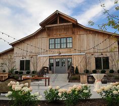 a large wooden building with white flowers in the foreground and string lights strung across it