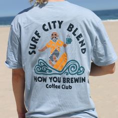 Named after our second location on LBI, the Surf City Blend is a favorite. Featuring a fun, graphic-style back design that captures a surfer drinking coffee on the waves. The ultimate classic tee - inspired by the casual-cool vibe from California, its design offers a retail fit. Enjoy the fit and style of this classic short sleeve in Stonewash Denim! Fabric Platform: 100% Cotton Jersey Fabric: 100% Combed Ring-Spun Cotton Collar: Crew Neck Fit Type: Classic Graphic Tee T-shirt For Surfing With Relaxed Fit, Relaxed Fit Graphic Tee For Surfing, Graphic Tee With Relaxed Fit For Surfing, Surfing Graphic Tee With Screen Print, Graphic Surfing T-shirt With Screen Print, Surfing Graphic Print Relaxed Fit T-shirt, Relaxed Fit Surfing T-shirt With Graphic Print, Graphic Tee With Screen Print For Surfing, Surfing Graphic Print Crew Neck T-shirt