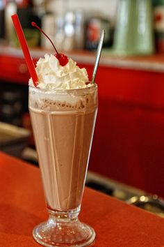 a chocolate drink with whipped cream and cherries in a tall glass on a counter