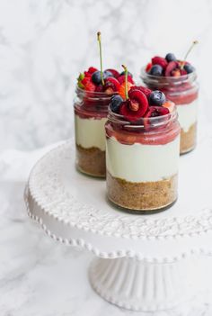 three small desserts with berries and whipped cream on a white cake platter next to a marble background