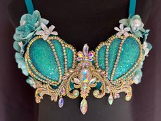 Dive into a world of aquatic magic with our stunning Aqua and Teal Glittery Mermaid Bra Top. This exquisite piece combines mesmerizing colors and dazzling embellishments to create a truly enchanting look. Designed for those who dare to embrace their inner mermaid, this bra top features a captivating blend of aqua, teal, and blue iridescent glitter shells. Each shell glistens and shimmers in the light, showcasing the beauty of the underwater realm. The gold accents add a touch of elegance, complementing the vibrant colors with a hint of glamour. Adorned with delicate aqua and teal silk flowers, this mermaid bra top exudes a whimsical charm that is sure to turn heads. The iridescent crystals, crystal chain, rhinestones, pearls, and jewels create a mesmerizing cascade of sparkle, adding depth Orange Mermaid Top, Mermaid Bras, Mermaid Bra Top, Mermaid Headdress, Mermaid Shell Bra, Underwater Realm, Sparkle Crafts, Bra Art, Orange Mermaid