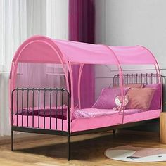 a child's bed with a pink canopy over it and pillows on the floor