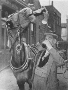 an old black and white photo of a man drinking from a bottle next to a horse