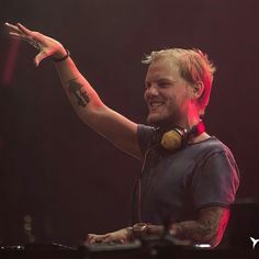 a man with headphones on holding his hand up in the air while standing next to a keyboard