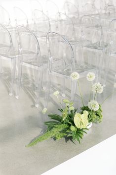 a bunch of clear chairs sitting next to each other with flowers in the middle of them