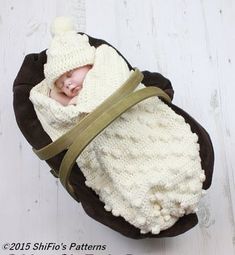 a baby wrapped up in a blanket on top of a white wooden floor next to a brown ribbon