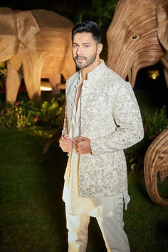 a man standing in front of an elephant statue wearing a white suit and tan tie