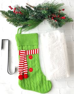 a green christmas stocking hanging on a brick wall next to a white towel and pine branch