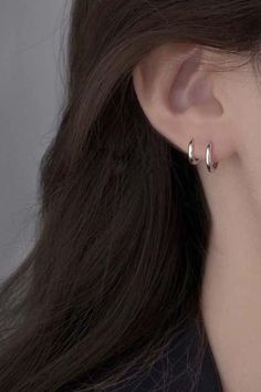 a close up of a woman's ear with two small silver hoop earrings on it