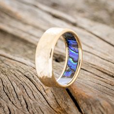 a wedding ring with an opal inlay sitting on top of a piece of wood