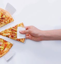 a hand holding a piece of pizza with cheese and tomatoes on it, next to three slices of pizza