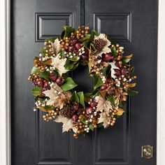 a wreath on the front door with pine cones, berries and other autumn foliages