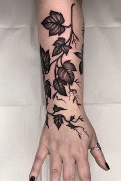 a woman's hand with black flowers and leaves tattoo on it, while she is holding