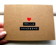 a hand holding a card with the words hello handsome written on it and a red heart