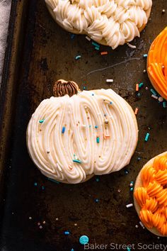 three pumpkins with white frosting and sprinkles on a baking sheet